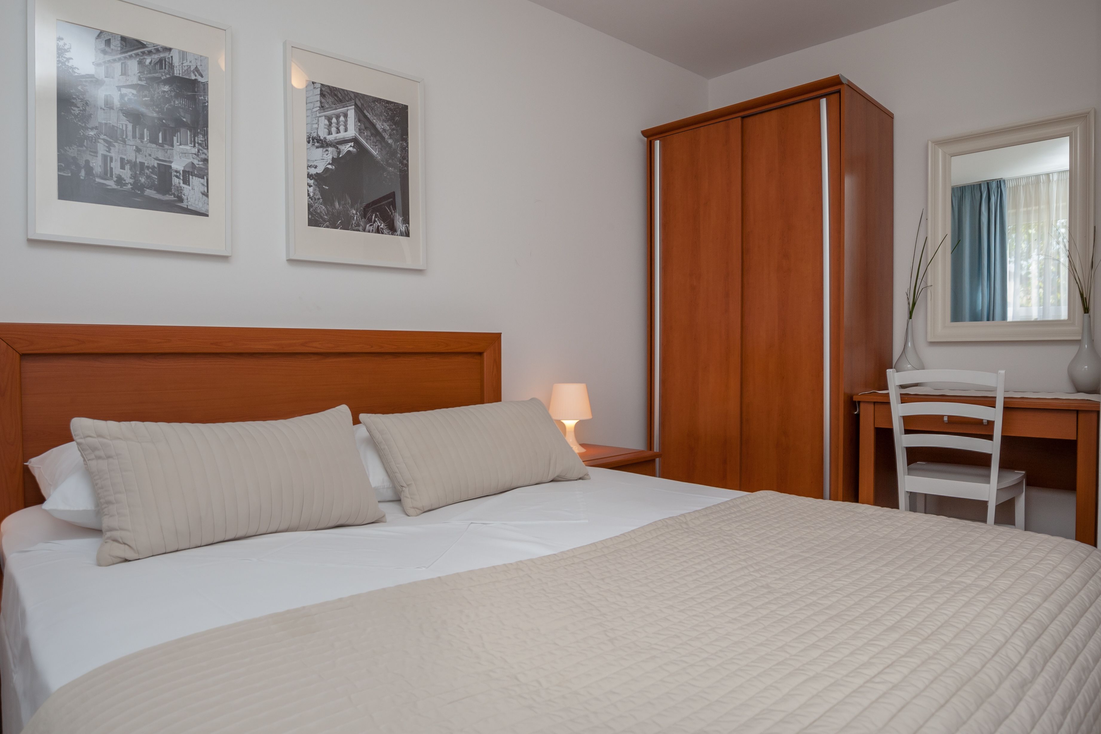 Un lit bien fait, avec une tête de lit en bois, un bureau avec une chaise et deux tableaux encadrés accrochés au mur.