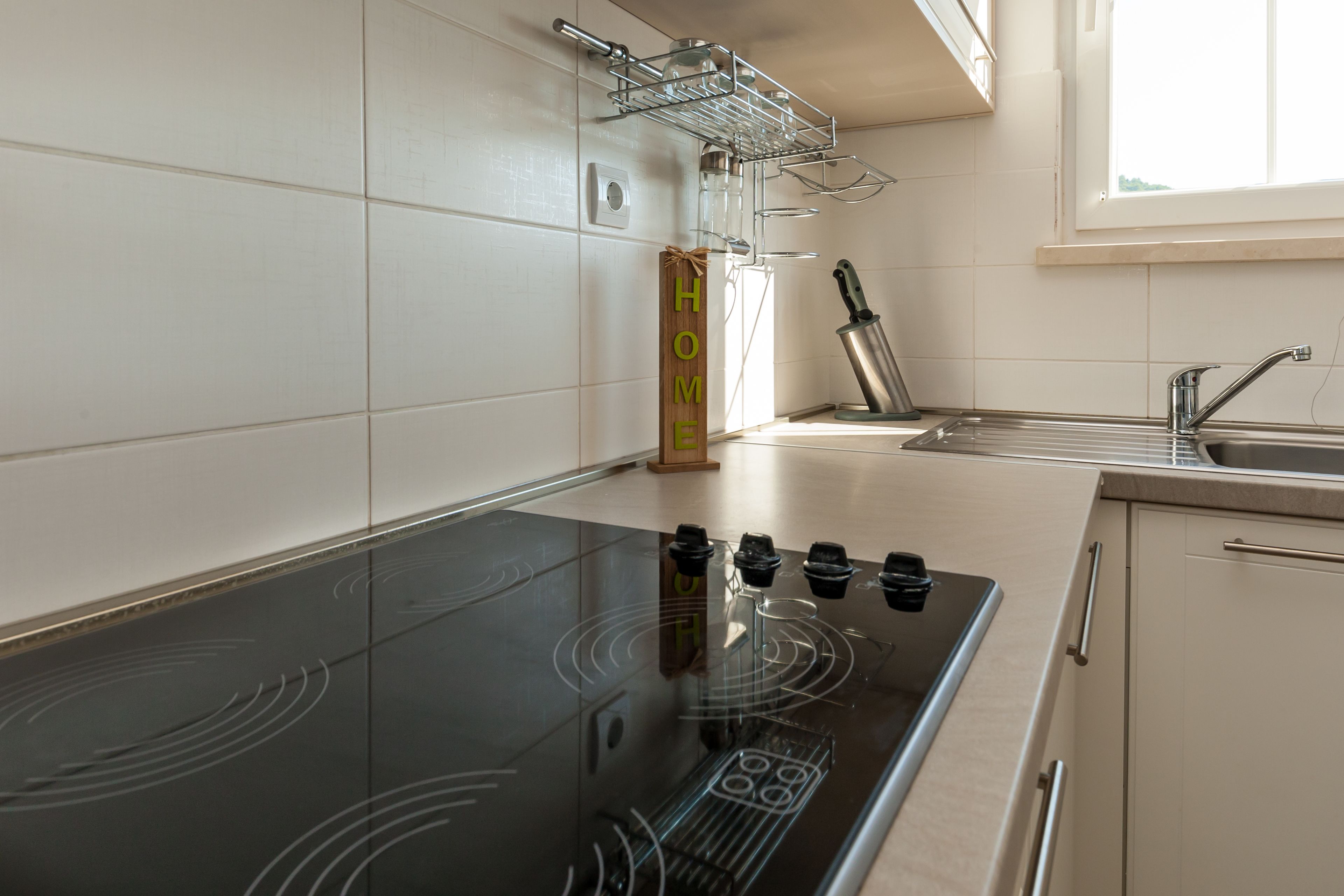 A modern kitchen with a black induction cooktop, a stainless steel sink, and a window above the sink.