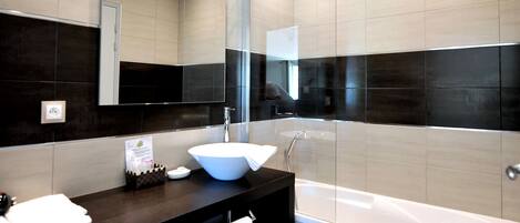 A modern bathroom with a dark wood vanity, a white sink, a large mirror, and a bathtub.