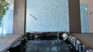 Une salle de bain moderne avec une grande baignoire sur pieds, une barre d’appui et un mur recouvert de carreaux formant une mosaïque bleue.