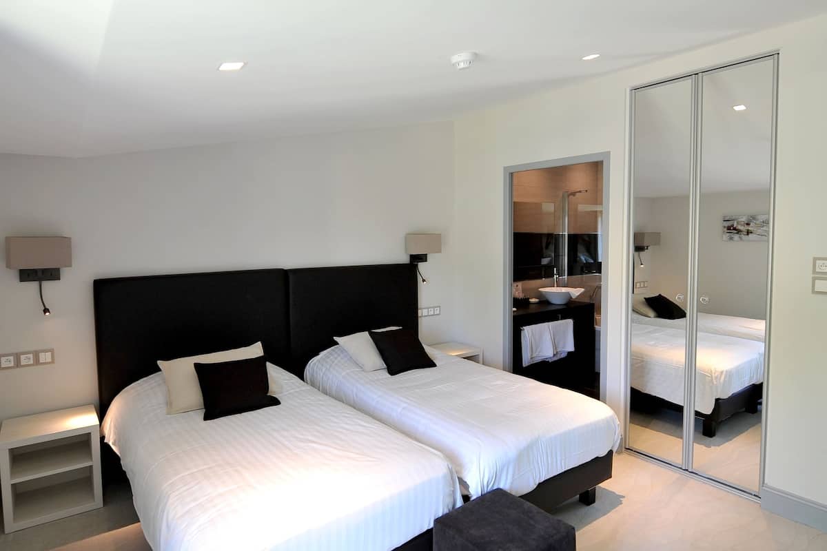 Une chambre moderne avec deux lits, un grand miroir et un dressing.