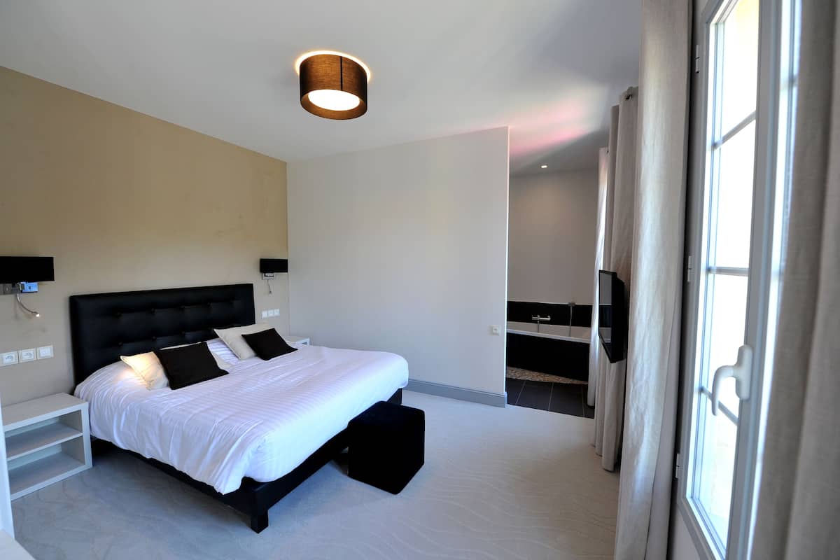 Une chambre d’hôtel moderne avec un grand lit, des tables de chevet, une télévision et une fenêtre avec des rideaux.