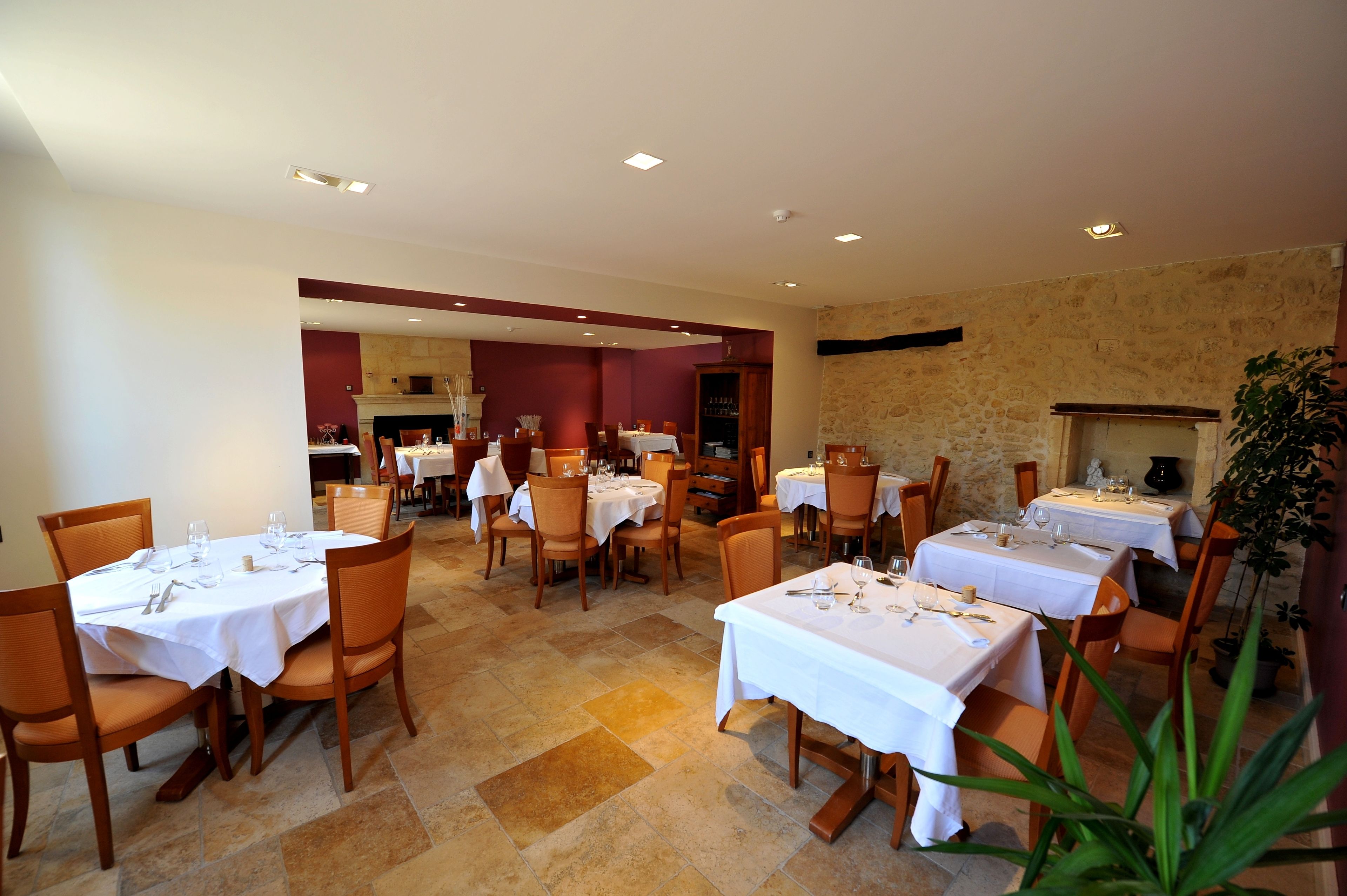 A restaurant with multiple tables set for dining, featuring a stone wall and a fireplace.