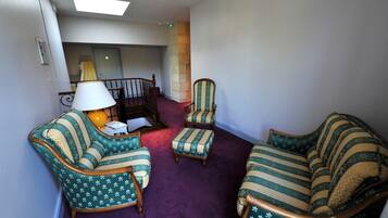 A room with a purple carpet, two striped armchairs, a small table with a lamp, and a staircase in the background.