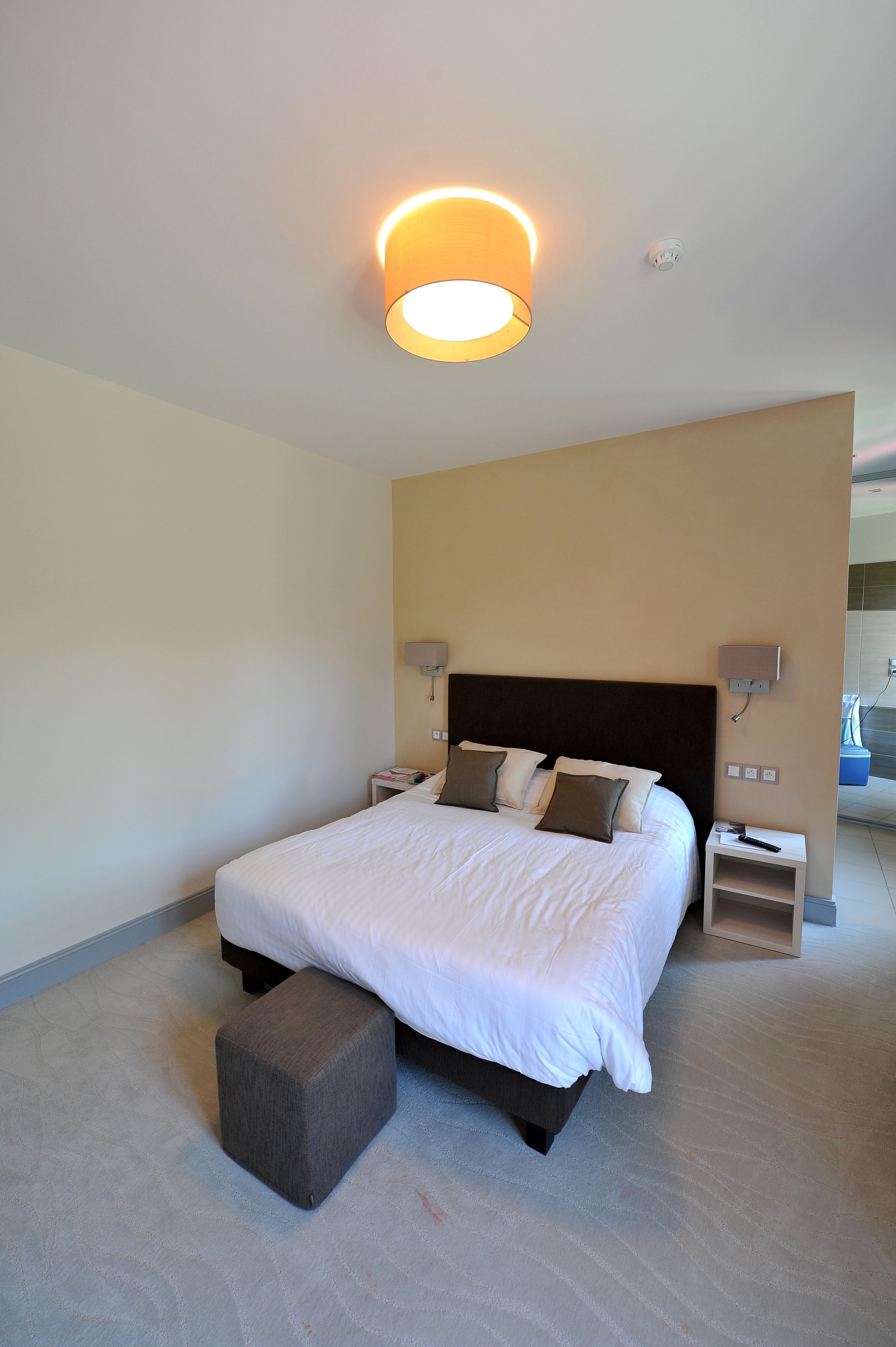 Una habitación de hotel moderna con una cama grande, lámparas de noche, una mesita y una luz en el techo.