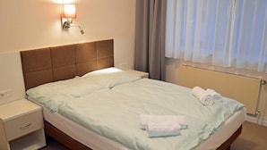 A hotel room with a bed, a nightstand, a lamp, and a window with curtains. - G&H Hotel Rosengarten (Rosengarten)