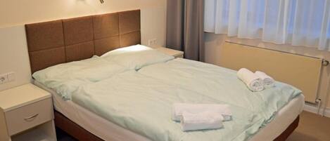 A hotel room with a bed, a nightstand, a lamp, and a window with curtains.