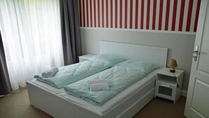 A single-bed room with a white headboard, a bedside table with a lamp, and a window with curtains. - G&H Hotel Rosengarten (Rosengarten)