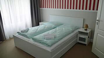 A single-bed room with a white headboard, a bedside table with a lamp, and a window with curtains.