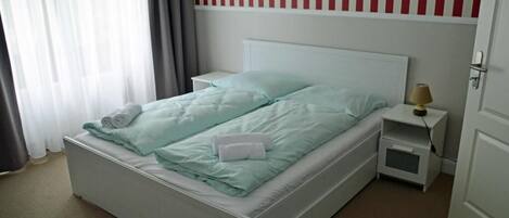 A single-bed room with a white headboard, a bedside table with a lamp, and a window with curtains.