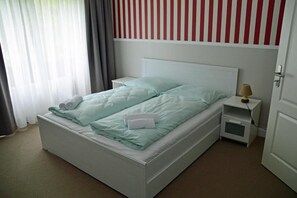 A single-bed room with a white headboard, a bedside table with a lamp, and a window with curtains. - G&H Hotel Rosengarten (Rosengarten)