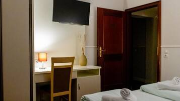 A hotel room with a bed, a desk with a chair, a television, and a wardrobe.