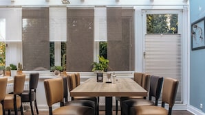 A dining area with a wooden table and leather chairs, surrounded by large windows with blinds. - G&H Hotel Rosengarten (Rosengarten)