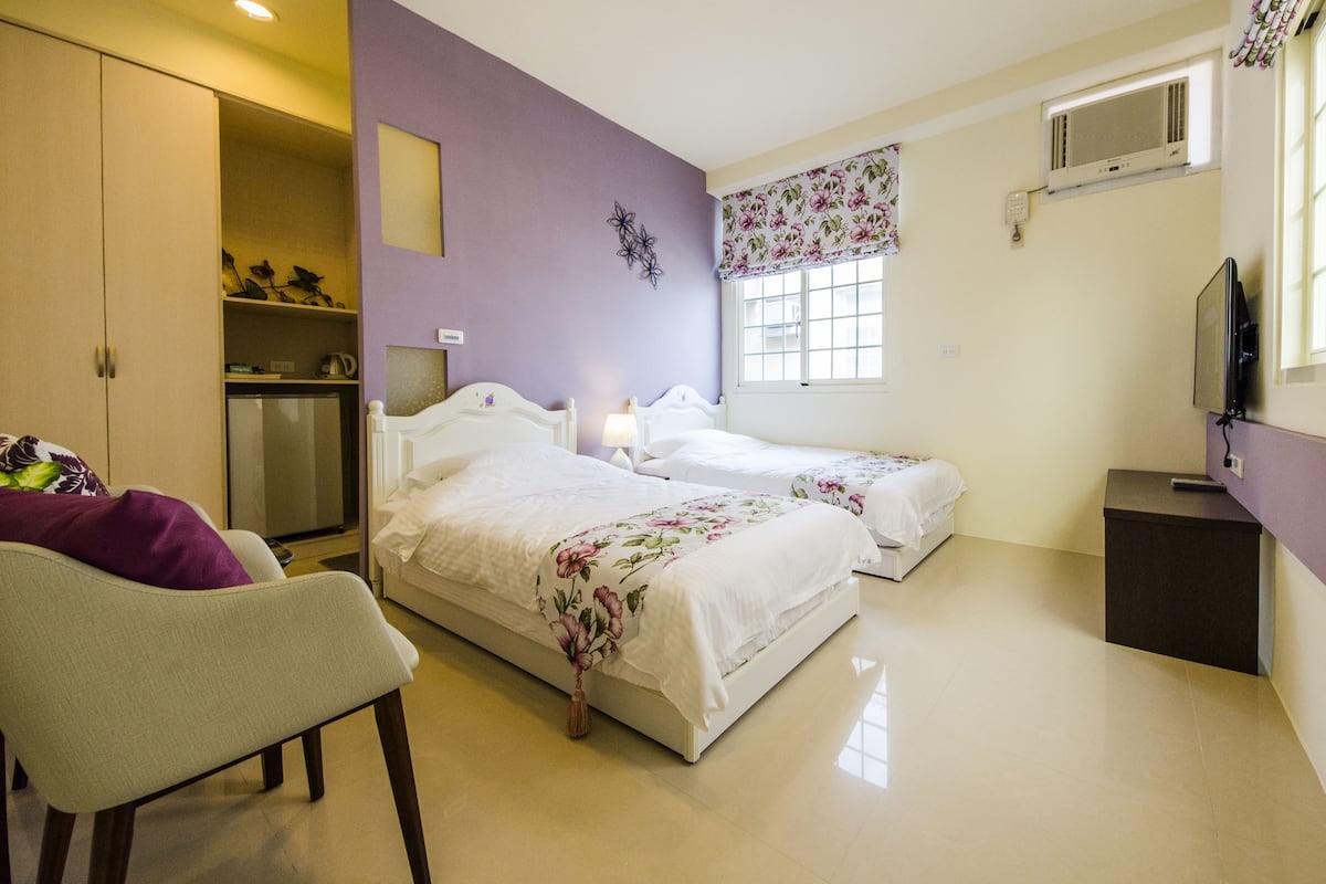 Quarto com duas camas, uma cadeira, escrivaninha, guarda-roupa e televisão.