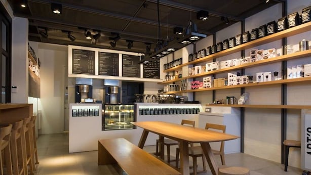 A modern cafe interior with wooden furniture, a display of coffee products, and a menu board. - White House Asoke Sukhumvit 18 (Bangkok)