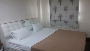 A bedroom with a bed, white bedding, a brown throw blanket, and a window with a tree pattern curtain. - White House Asoke Sukhumvit 18 (Bangkok)