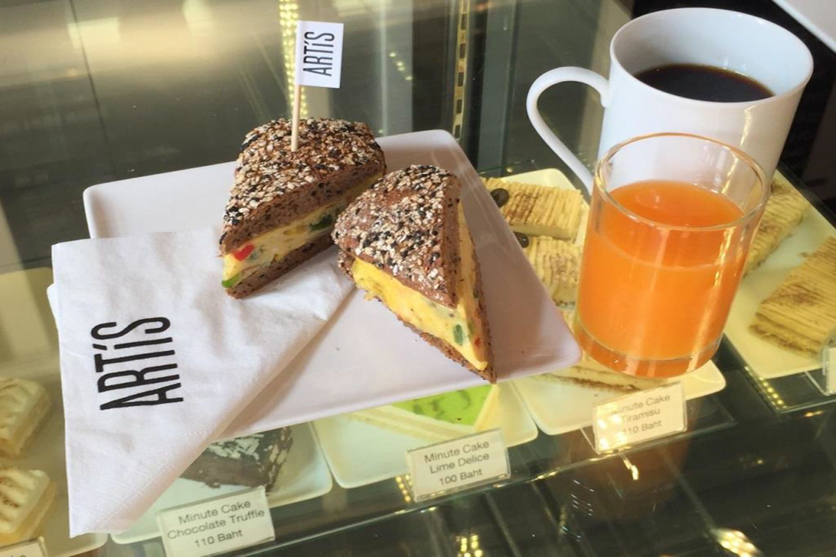 A dessert display with a sign reading "ARTIS" and a cup of coffee.