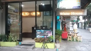 The exterior of a hotel named 'White House' with a glass entrance, a signboard advertising a 'Dinner Cruise', and outdoor seating area. - White House Asoke Sukhumvit 18 (Bangkok)