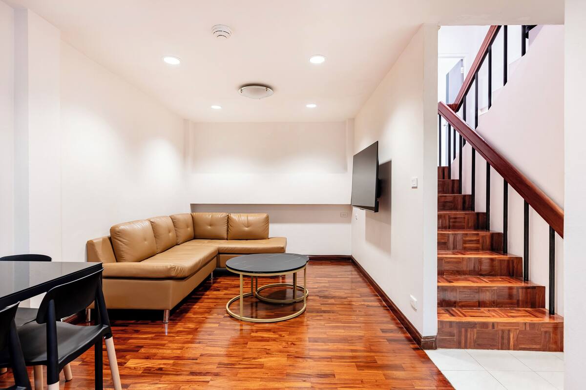 A modern living room with a leather sofa, a round table, and a staircase.