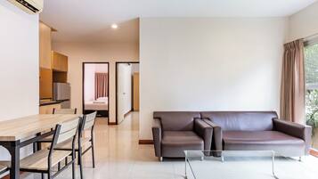 A modern living room with a glass coffee table, a brown leather sofa, and a dining area with a wooden table and chairs.