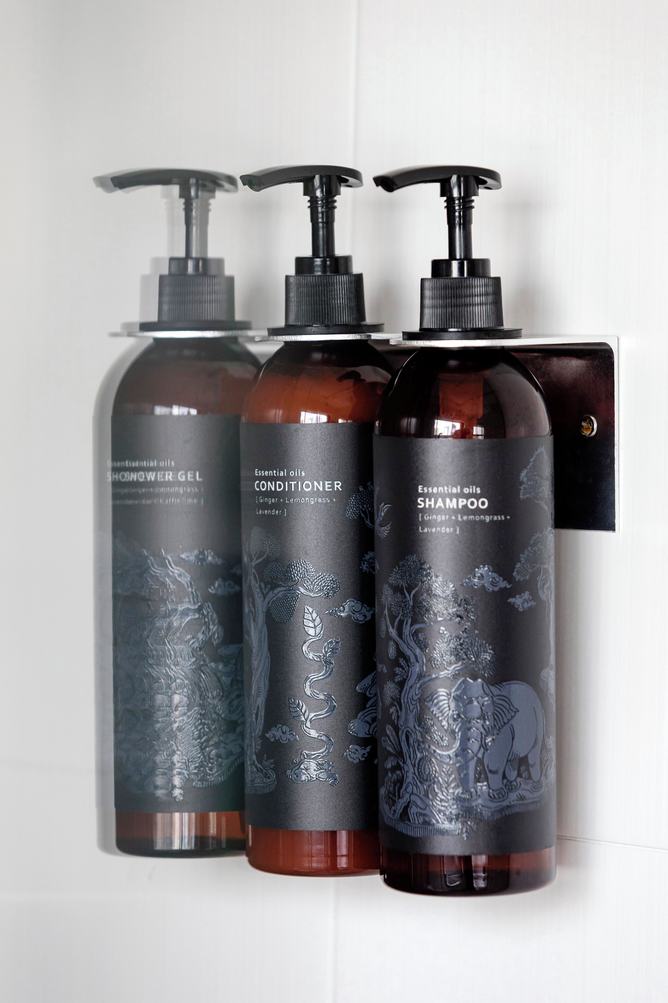 Three bottles of essential oils with pump dispensers, labeled as shower gel, conditioner, and shampoo.