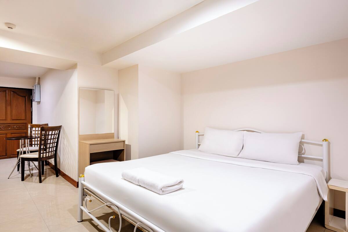 A hotel room with a neatly made bed, a desk with a chair, and a wooden cabinet.