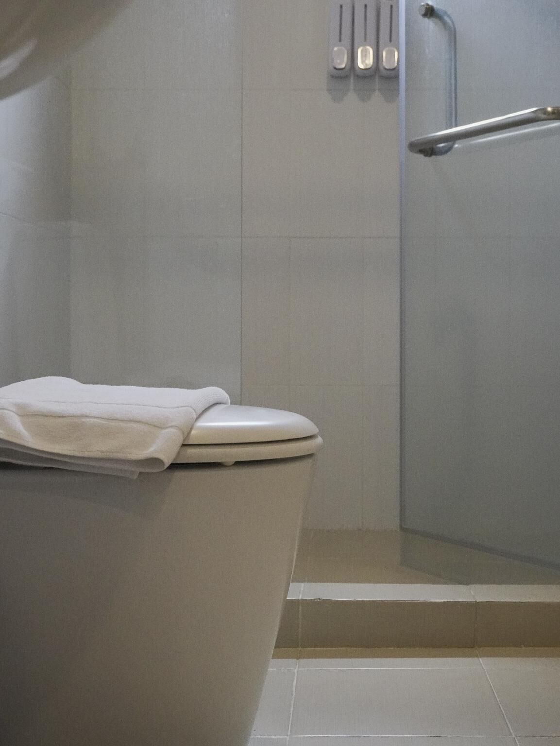 Un baño con inodoro, ducha y una toalla sobre el asiento del inodoro.