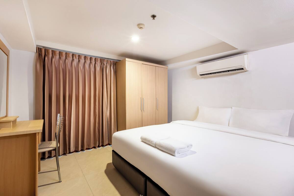 A hotel room with a bed, a desk, a chair, and a wardrobe.