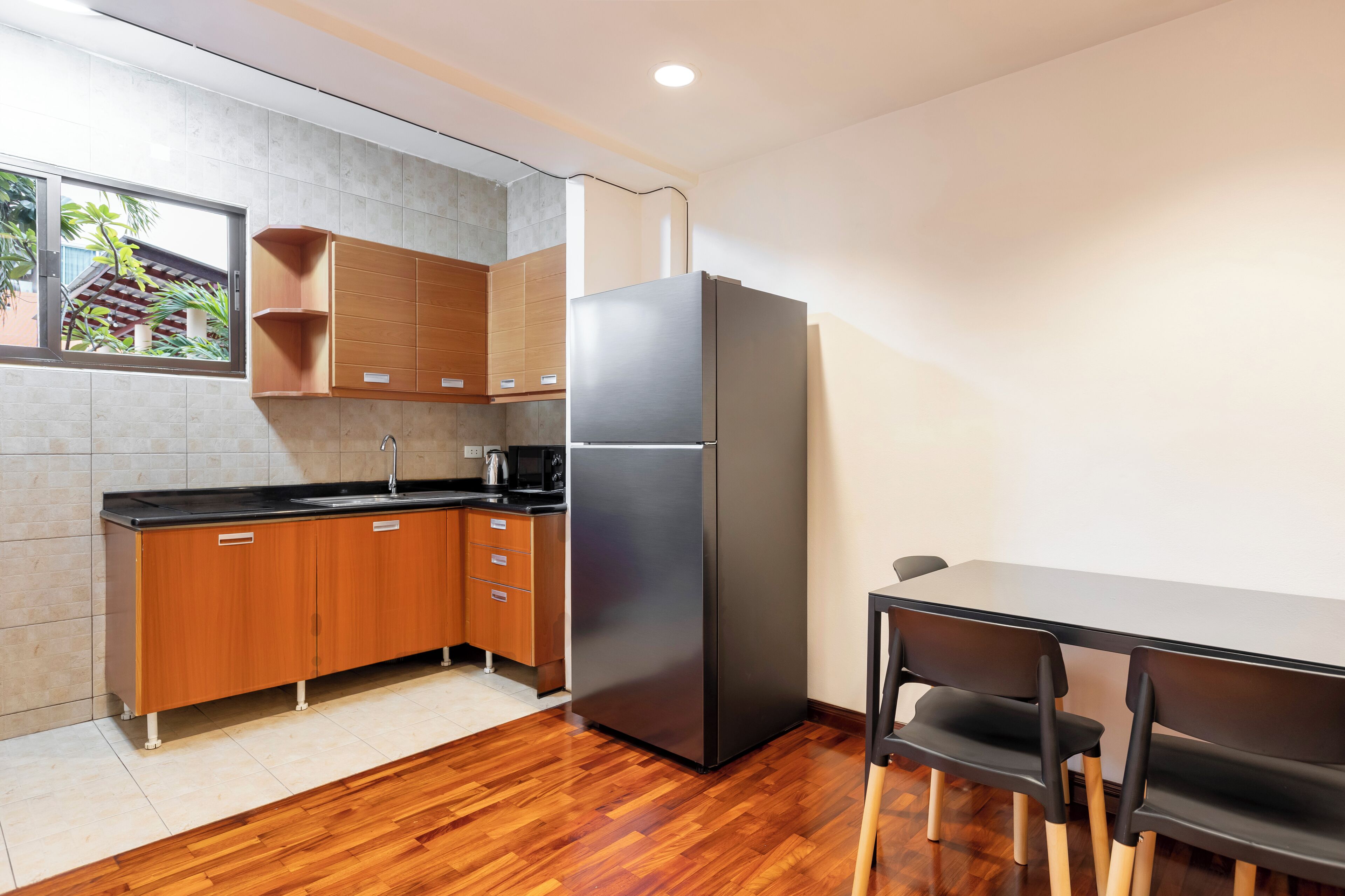 A modern kitchen with wooden cabinets, a black refrigerator, and a dining table with chairs.