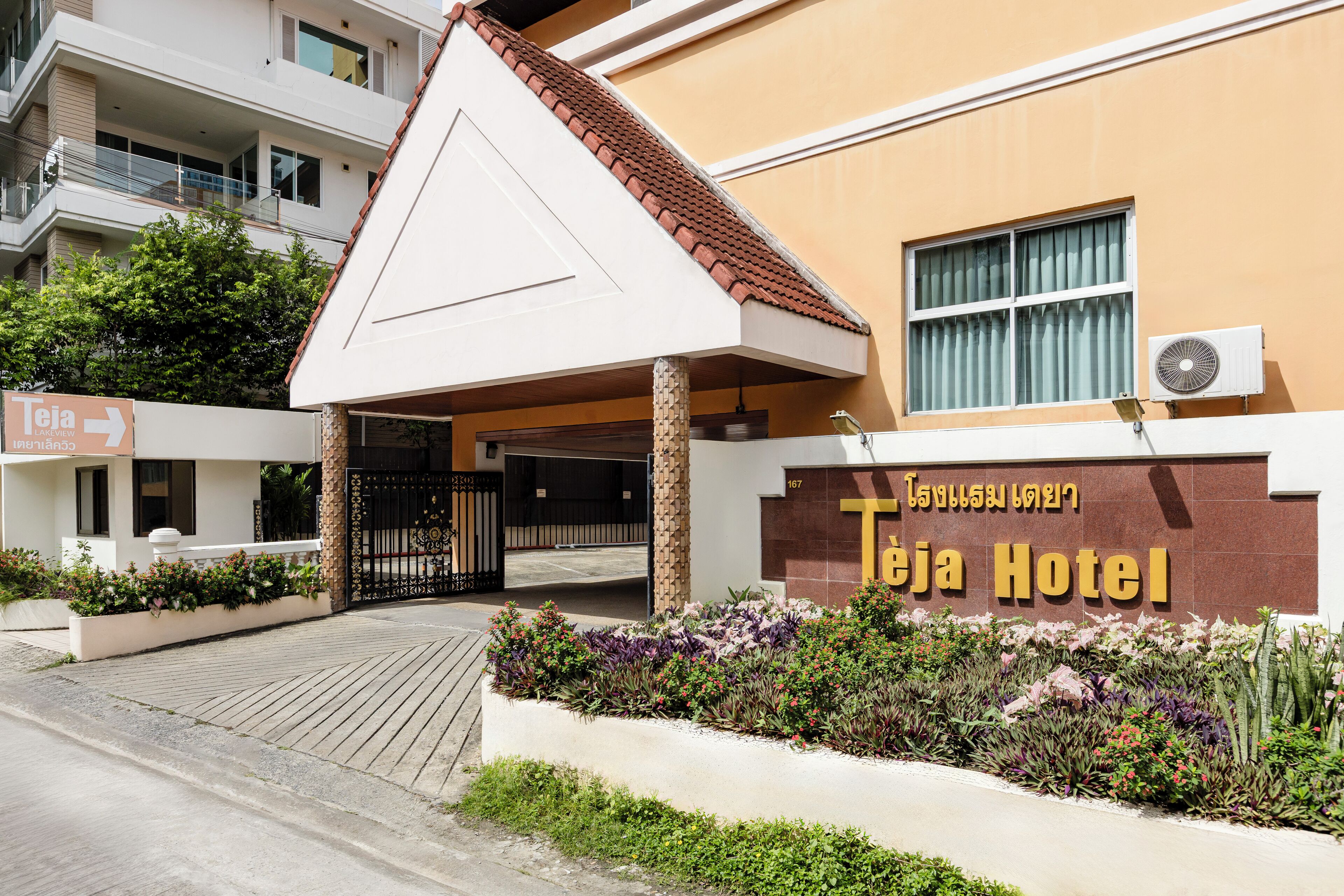 The exterior of Teja Hotel with a prominent entrance, a gated driveway, and a signboard.