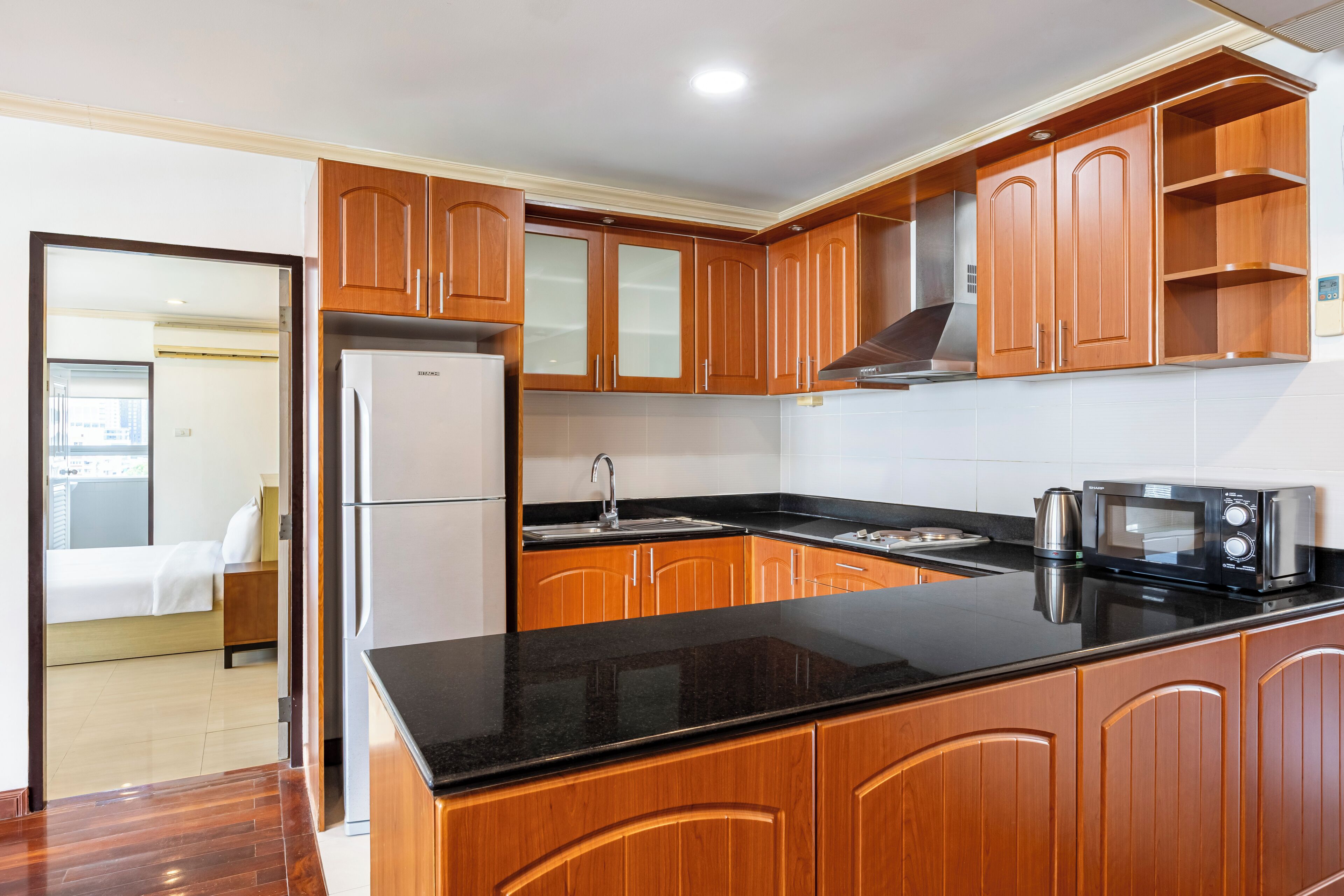 A modern kitchen with wooden cabinets, a black countertop, a stainless steel refrigerator, a microwave, and a kettle.