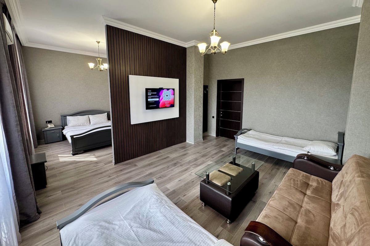 Una habitación de hotel moderna con una televisión de pantalla plana grande montada en la pared, una cama con cabecera de madera, un sofá, una mesita de centro pequeña y un armario.