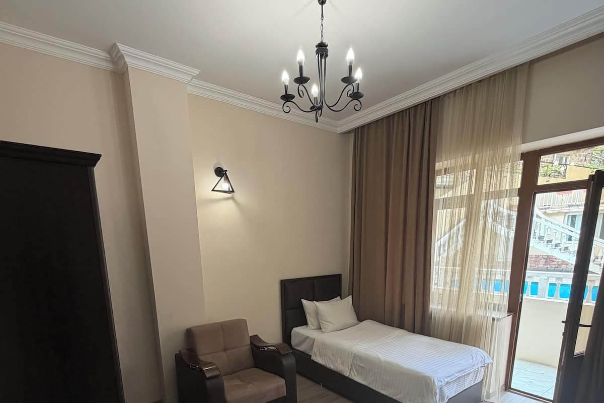 Habitación de hotel con cama, una silla, mesita de noche, lámpara y vistas al exterior.