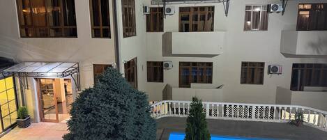 A multi-story building with a swimming pool, potted plants, and a covered outdoor seating area.