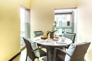 A dining area with a round table, wicker chairs, and a view of a building through a glass door. - Exe San Jose Center (San Jose)