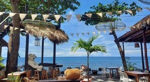 An outdoor seating area with tables and chairs, a thatched-roof structure, and a view of the ocean. - Warapura Resort (Ko Chang)