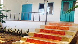 A staircase leading to a door with a blue frame, a window with a blue shutter, and a metal railing. - Sleepy Owl Hostel (Ko Chang)