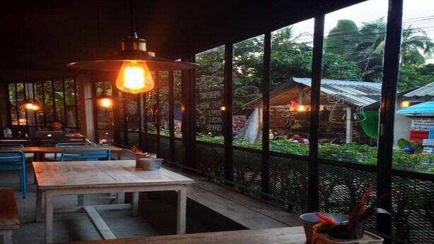 An indoor dining area with tables and chairs, large windows, and hanging pendant lights. - Sleepy Owl Hostel (Ko Chang)