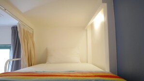 A small, single-bed room with a white bedspread and a colorful striped blanket. - Sleepy Owl Hostel (Ko Chang)