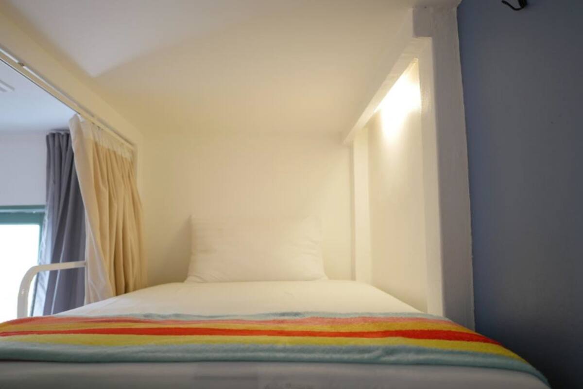 A small, single-bed room with a white bedspread and a colorful striped blanket.