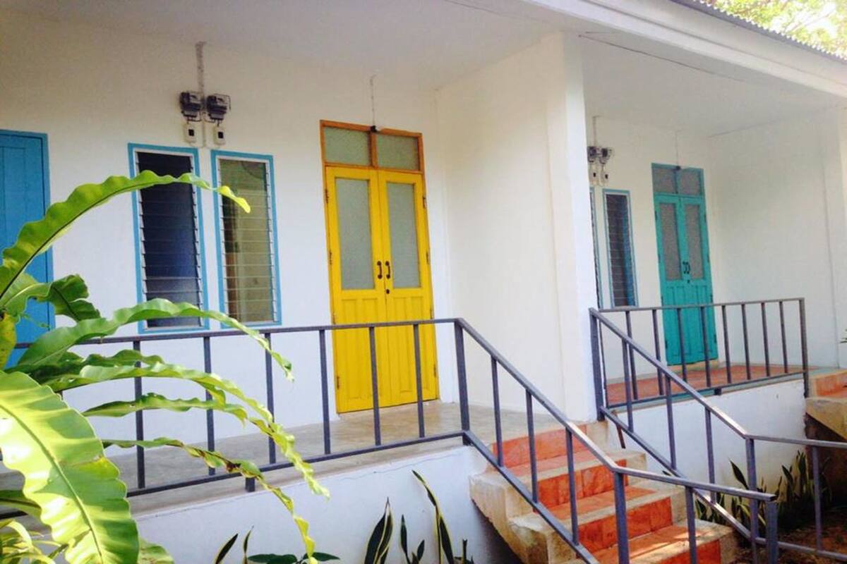 A building with a white exterior, a yellow door, and blue-framed windows. There is a staircase with metal railings leading to the entrance.