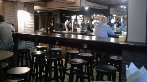 Een bar met krukken en tafels, een toonbank met personeel en een bakstenen muur.