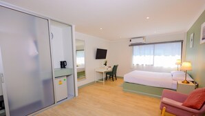 Een hotelkamer met een bed, bureau, stoel, kledingkast, televisie en een raam met gordijnen.