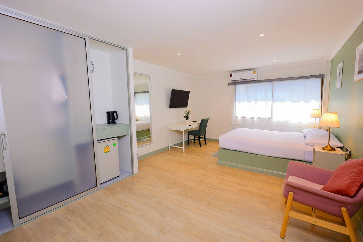 Une chambre d’hôtel équipée d’un lit, d’un bureau, d’une chaise, d’une armoire, d’une télévision et d’une fenêtre avec des rideaux.