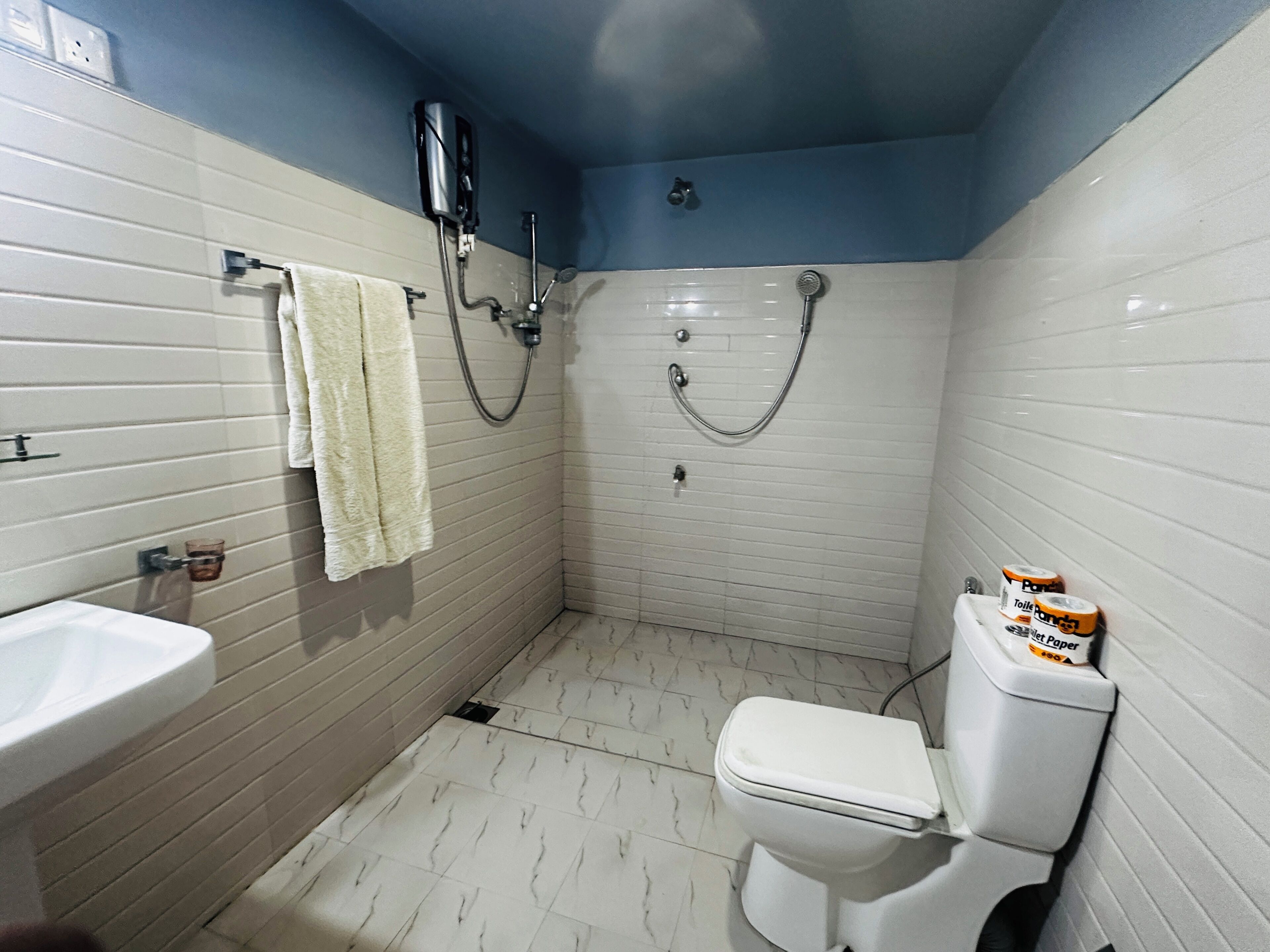 A bathroom with a white toilet, a sink, a shower with a handheld showerhead, and a towel hanging on the wall.