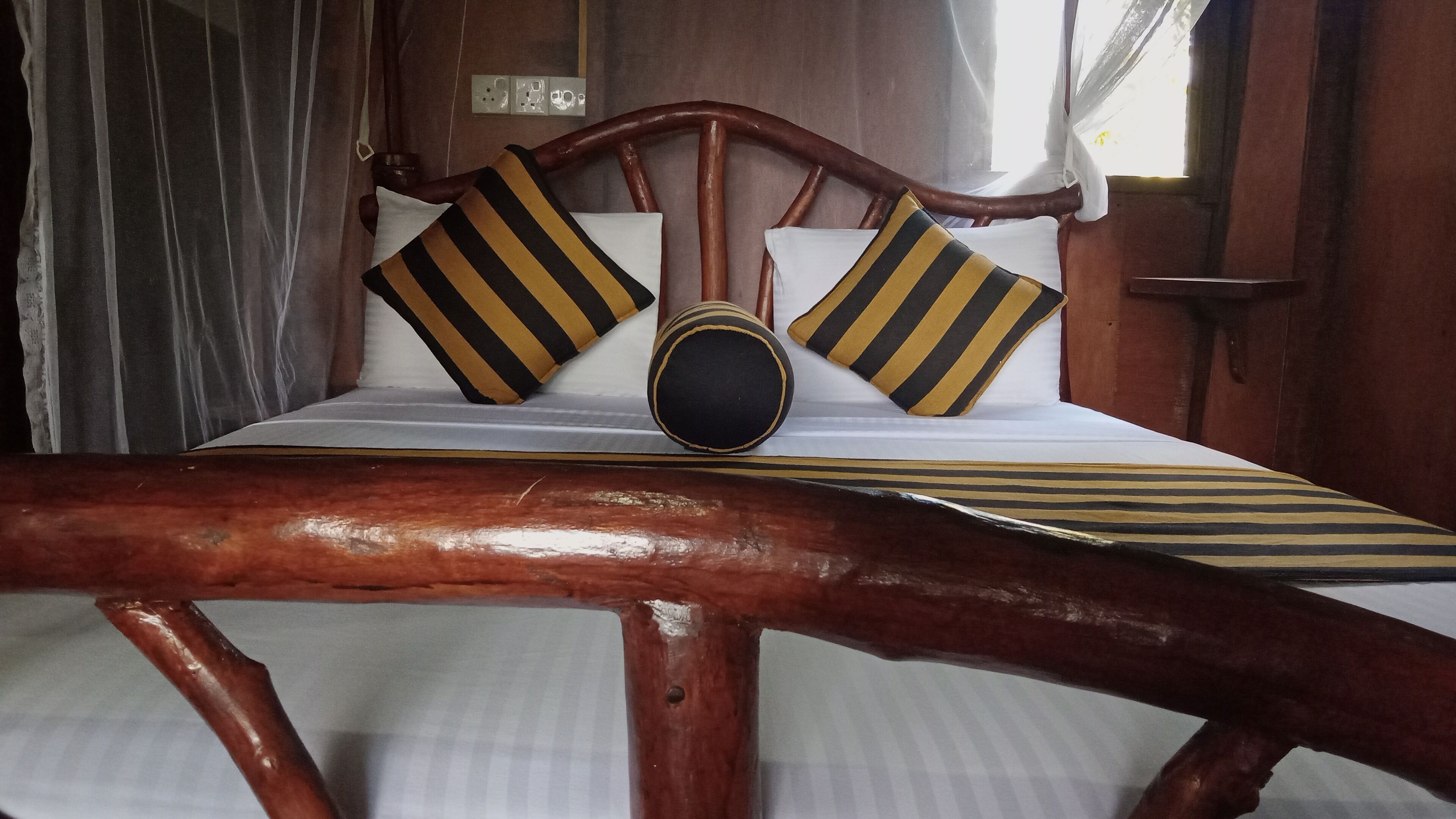 Una cama de madera con almohadas a rayas y un objeto decorativo redondo en la cabecera.