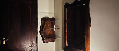 A room with a wooden door, a wall-mounted mirror, a small table with a lamp, and a wall socket.