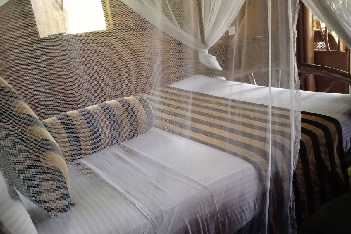 Quarto com cama coberta por mosquiteiro, sofá listrado e cabeceira de madeira.