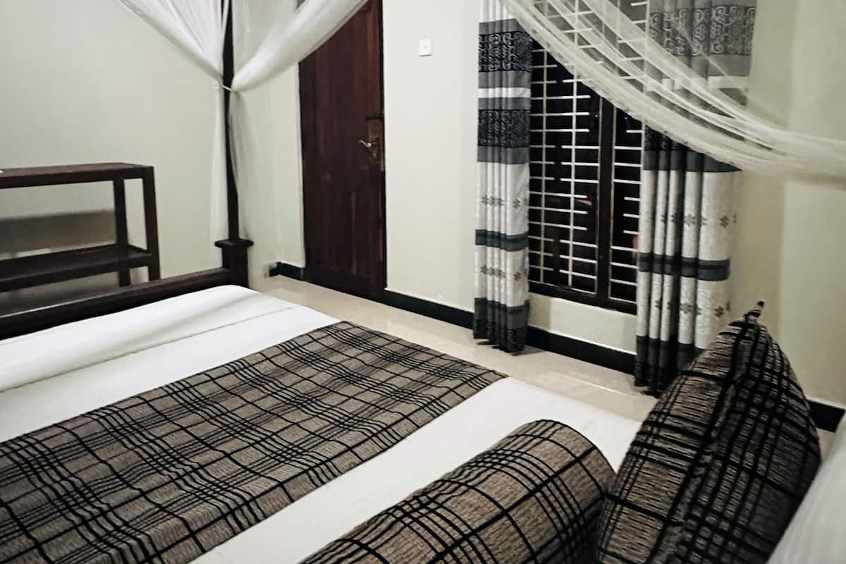 A bedroom with a bed, a wooden bench, a door, and a window with curtains.