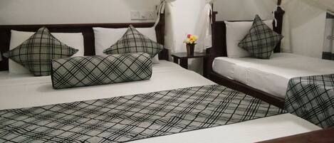 Una habitación de hotel con dos camas, cada una con colcha a cuadros y almohadas a juego. Entre las camas hay una mesita de noche con un jarrón de flores.